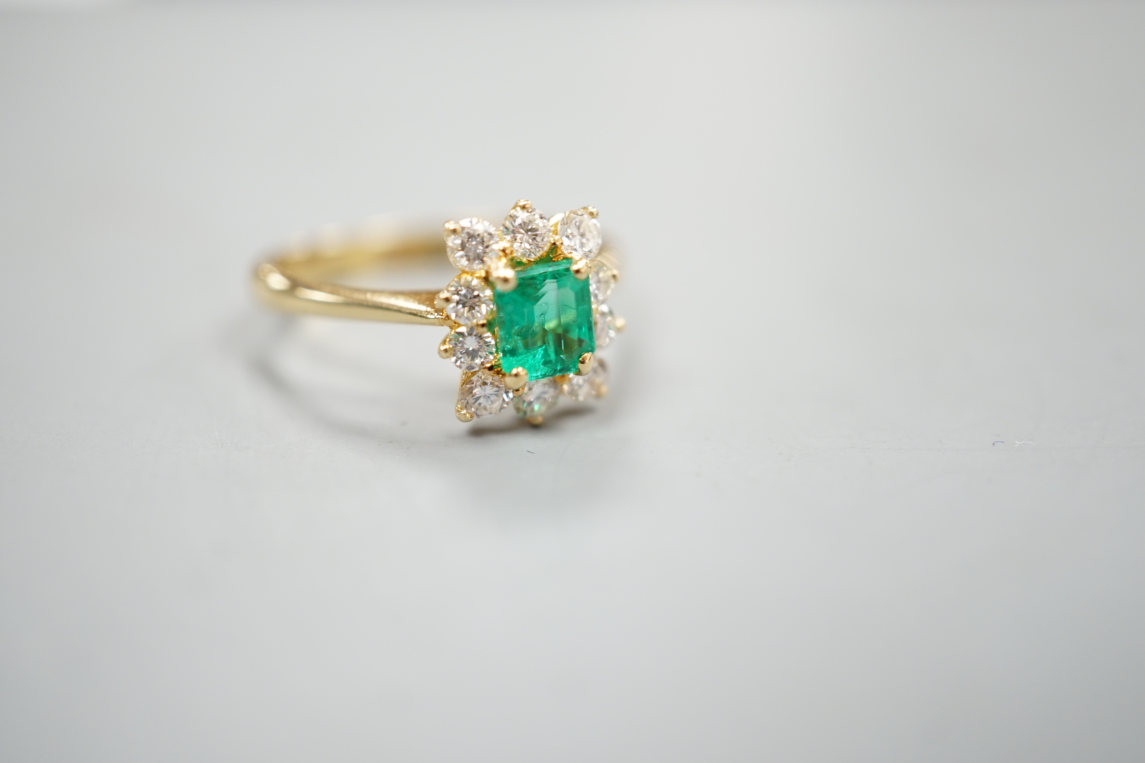 A 750 yellow metal, emerald and diamond set cluster ring, size m, gross weight 3.2 grams.